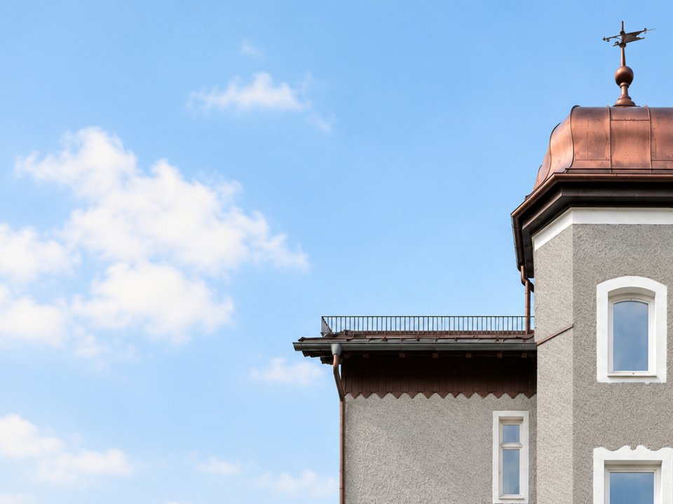 Detailansicht der denkmalgeschützten Villa mit Kupferkuppel und Wetterfahne vor blauem Himmel; im historischen Gebäude befinden sich unser Architekturbüro und Coworking-Bereich.