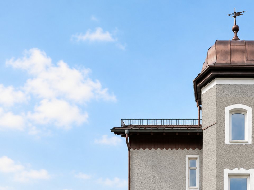 Detailansicht der denkmalgeschützten Villa mit Kupferkuppel und Wetterfahne vor blauem Himmel; im historischen Gebäude befinden sich unser Architekturbüro und Coworking-Bereich.